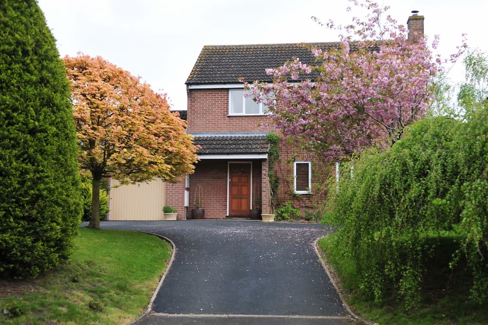 A newly installed tarmac driveway in front of a traditional UK semi detached house with a blossom tree outside of it
